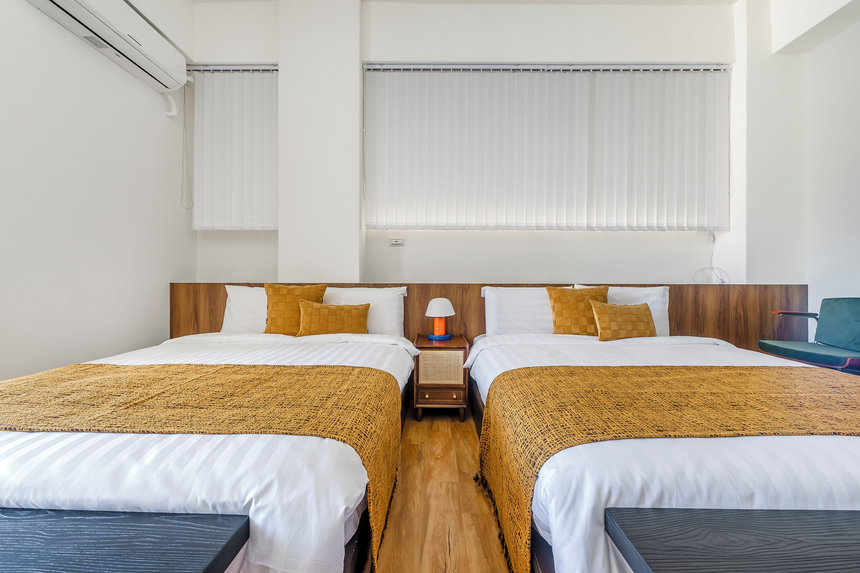 A hotel room with two beds, a nightstand with a lamp, and a view of the outside through the window.
