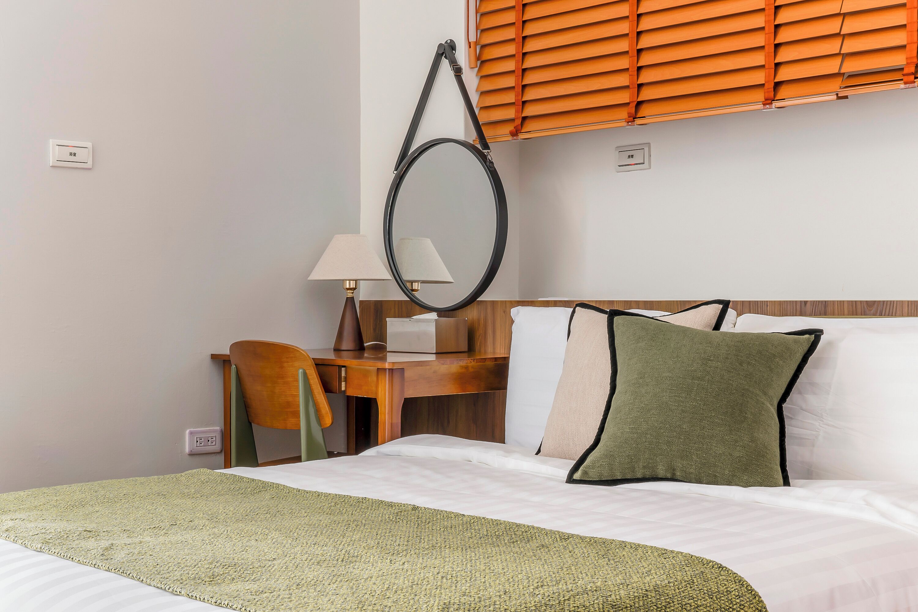 A hotel room with a bed, a desk, a chair, a lamp, and a window with blinds.