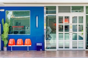 L’entrée d’un hôtel, avec un mur bleu, un comptoir d’accueil et un espace détente doté de chaises orange.