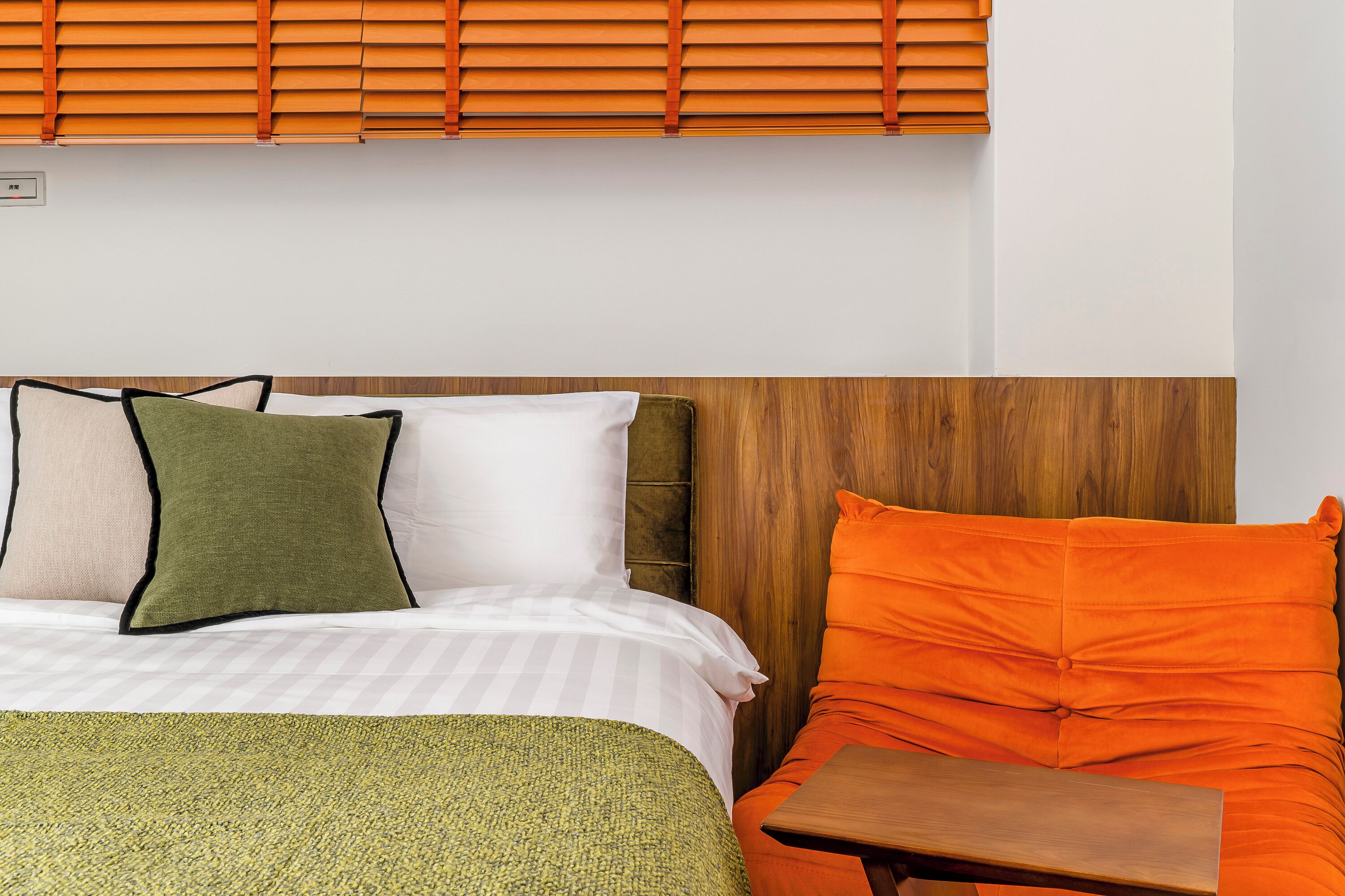 A hotel room with a bed, a wooden headboard, and a window with blinds.