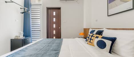 Una habitación de hotel con cama, mesita de noche, aire acondicionado en la pared, puerta y ventana con cortinas.