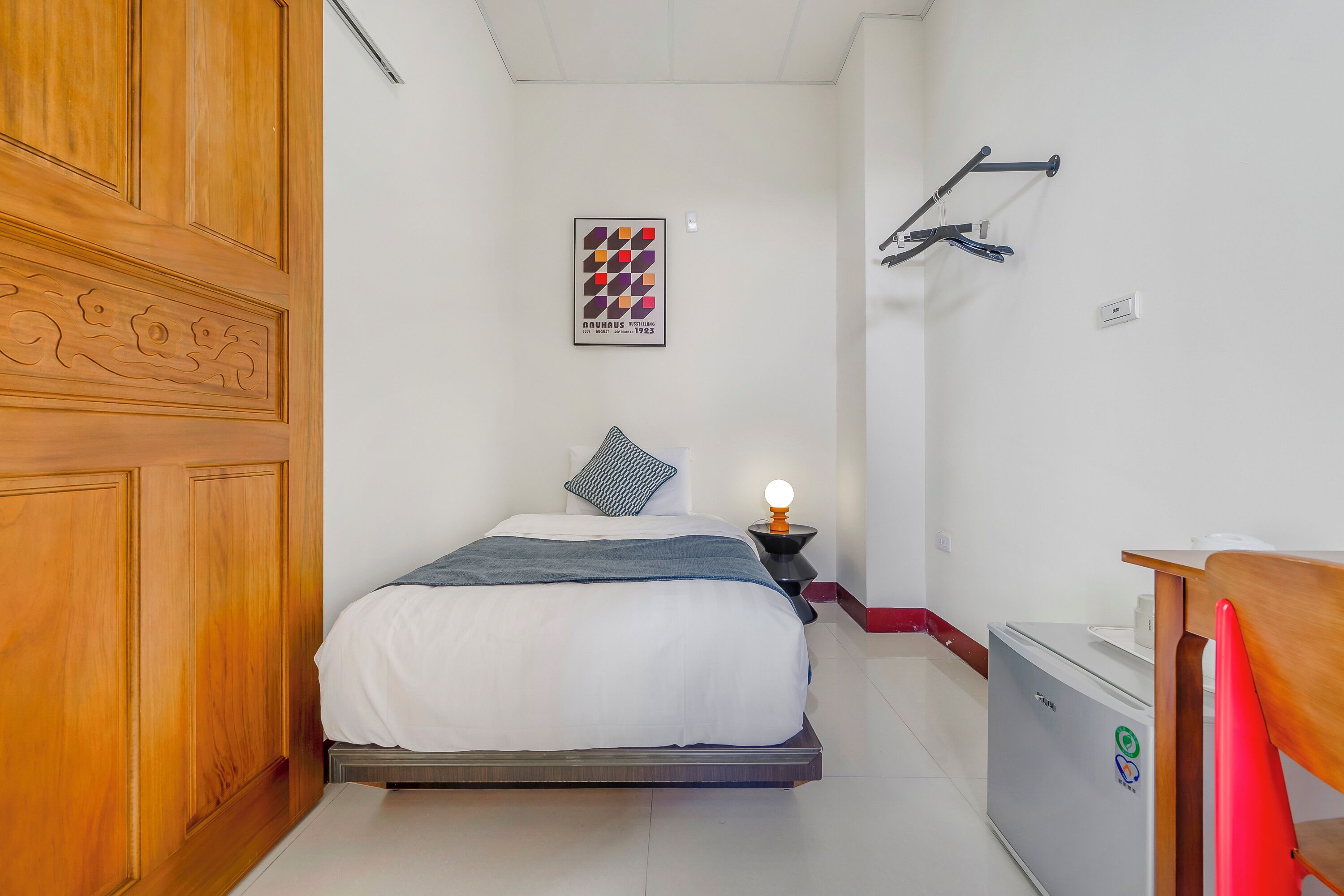 Un dormitorio con cama, mesita de noche, escritorio y refrigerador.