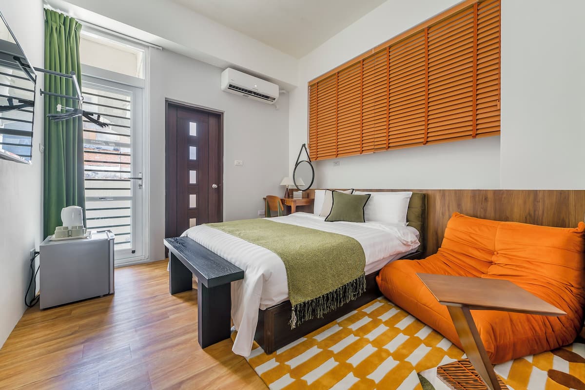 Une chambre à coucher comprenant un lit, un bureau, une chaise, une fenêtre avec des stores et un climatiseur fixé au mur.