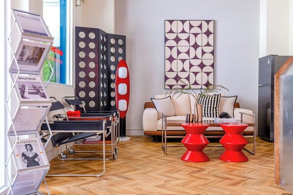 Un salon moderne avec un canapé, des tabourets rouges, une table basse et un grand tableau abstrait accroché au mur.