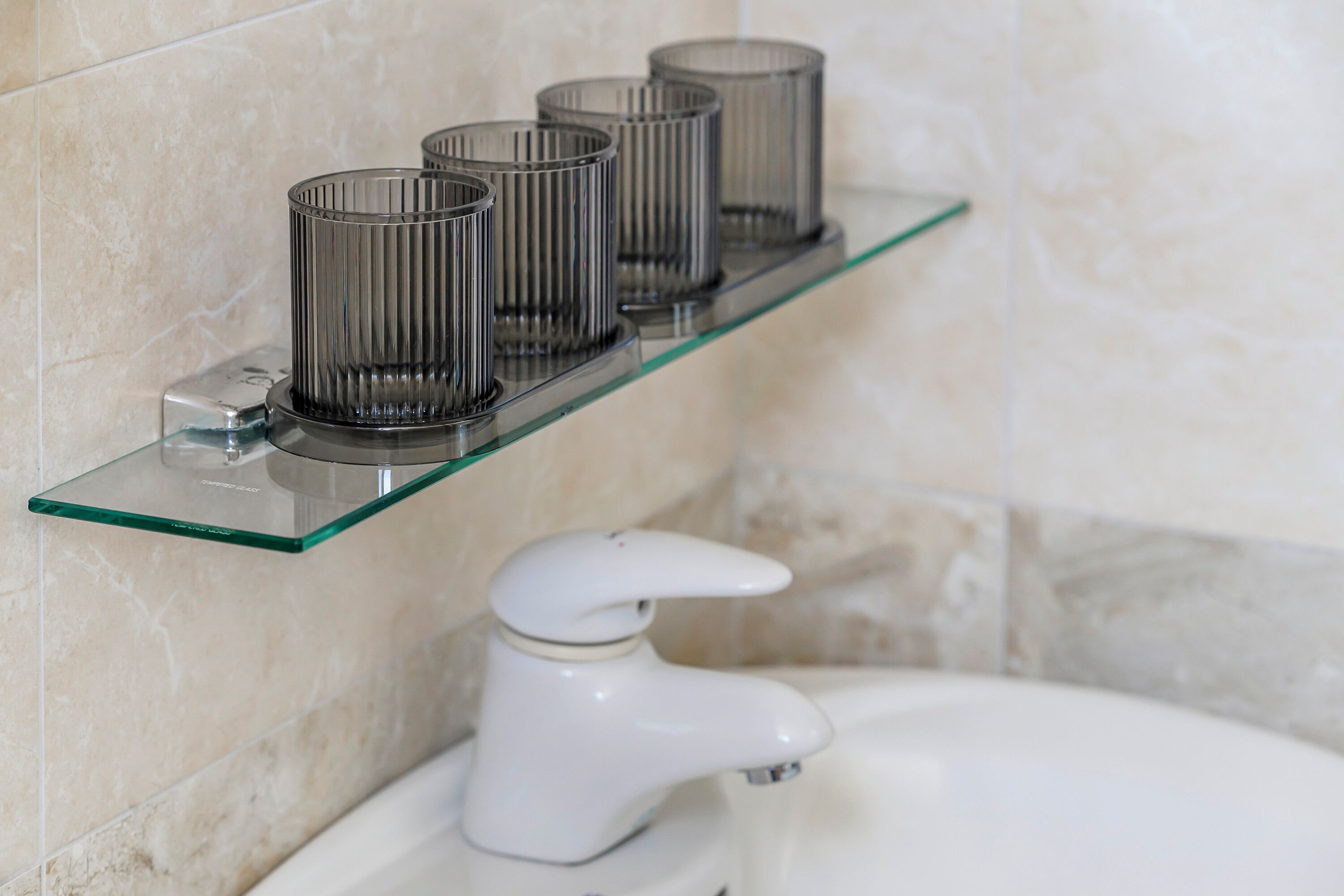 A bathroom with a glass shelf holding four cylindrical containers, a white faucet, and a white sink.