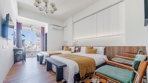 A modern hotel room with two beds, a desk, a chair, and a large window with blinds. - Oriental Blue Smart Stay (Taitung)