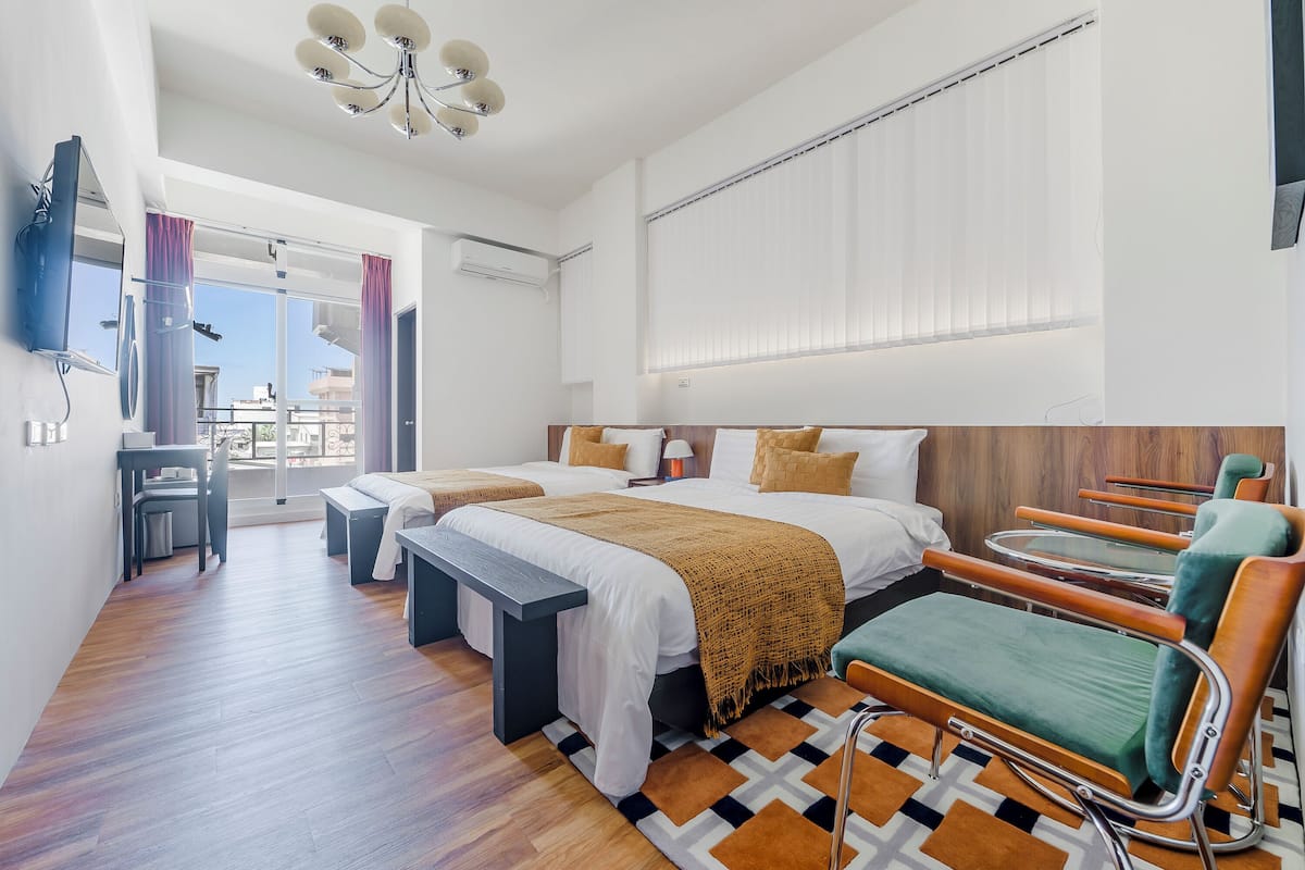 Une chambre d’hôtel moderne équipée de deux lits, d’un bureau, d’une chaise et d’une grande fenêtre avec stores.