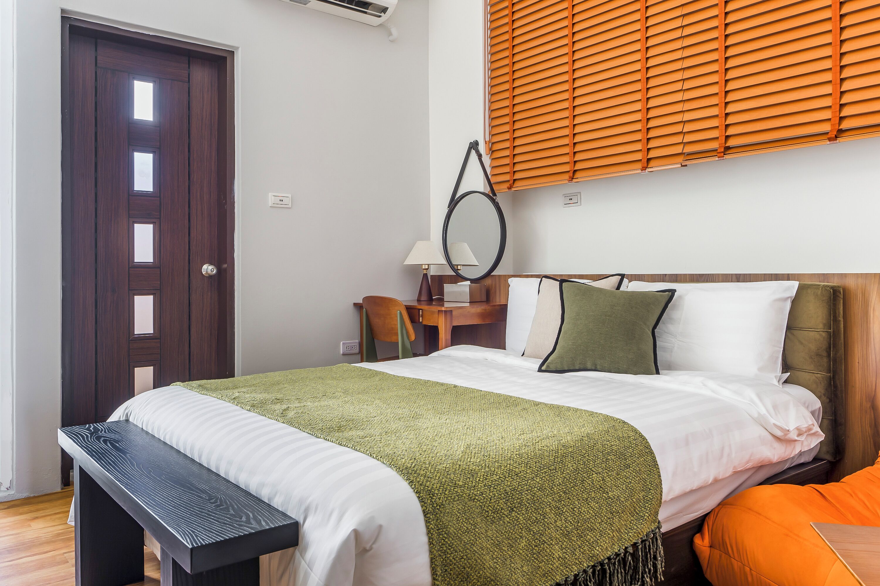 A hotel room with a bed, a desk, a chair, and a window with blinds.