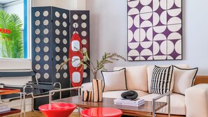 A modern living room with a sofa, coffee table, and red accent chairs. There is a bookshelf, a decorative vase, and a framed artwork on the wall. - Oriental Blue Smart Stay (Taitung)