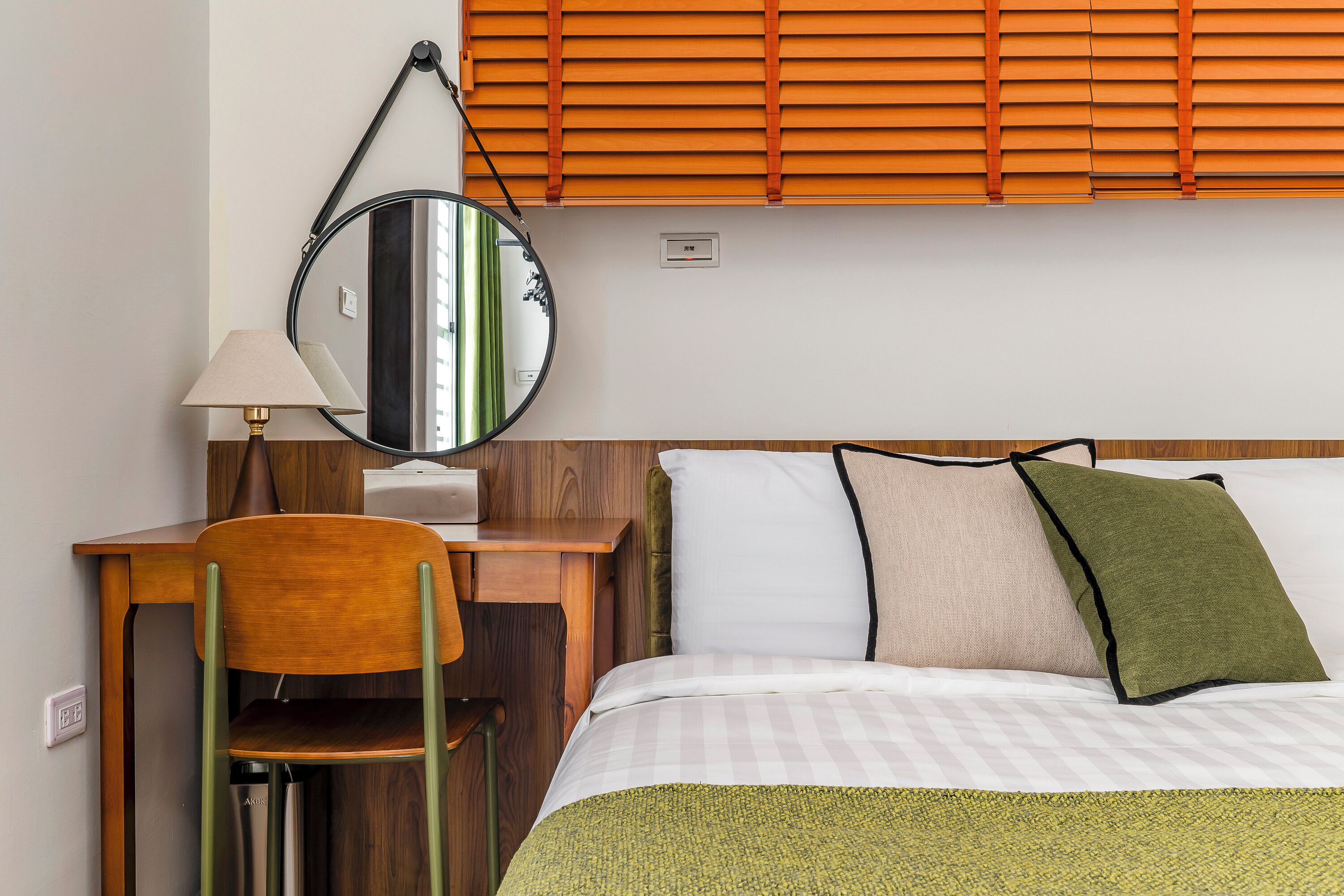 A hotel room with a bed, a desk, a chair, a lamp, and a window with blinds.