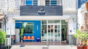 A hotel entrance with a blue facade, a sign above the door, and a small outdoor seating area with orange chairs. - Oriental Blue Smart Stay (Taitung)