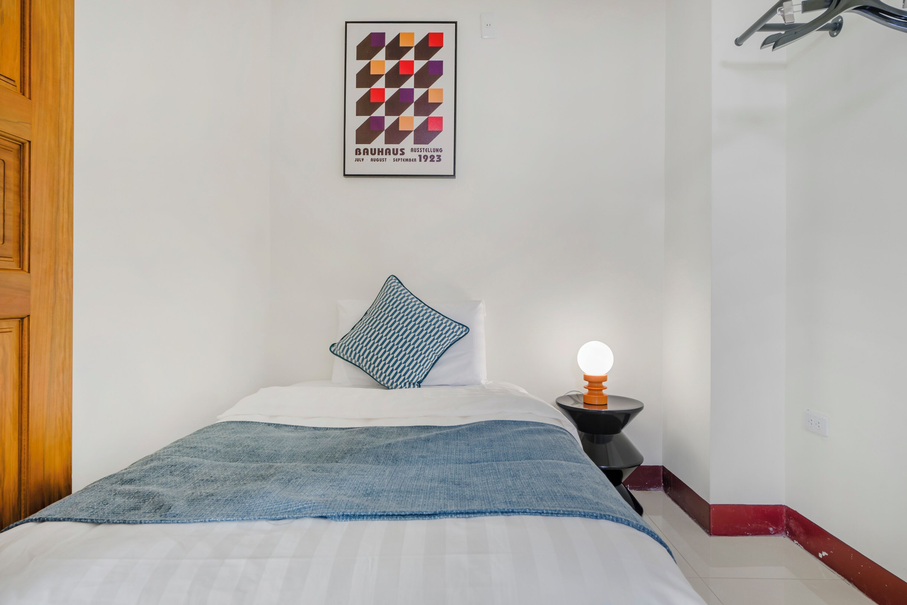 A neatly made bed with a blue blanket, a pillow, and a wall-mounted light.