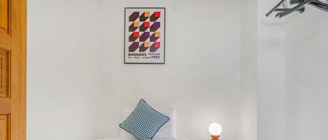 A neatly made bed with a blue blanket, a pillow, and a wall-mounted light.