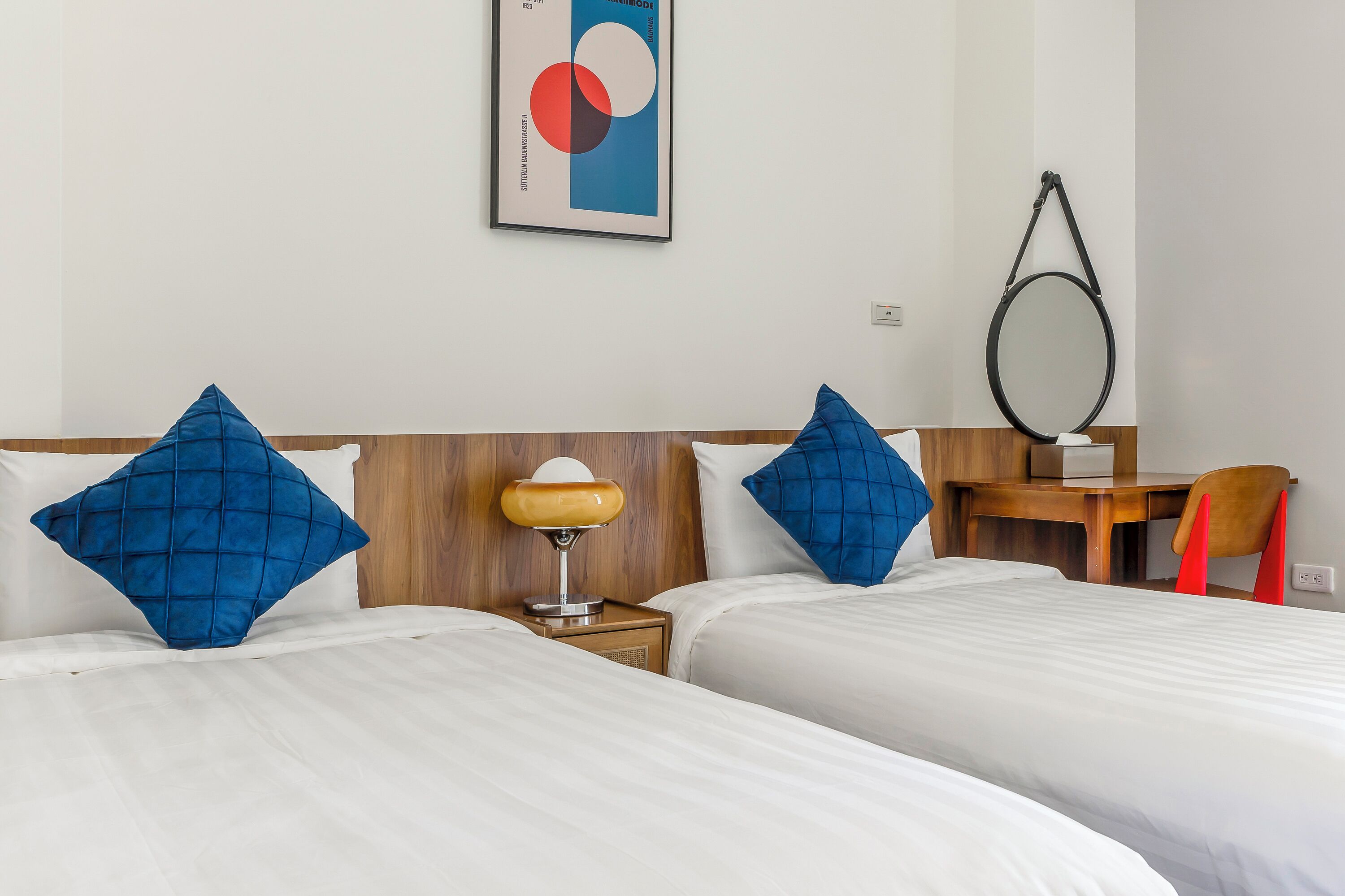 Une chambre d’hôtel avec deux lits, un bureau, une chaise, une lampe et un miroir.