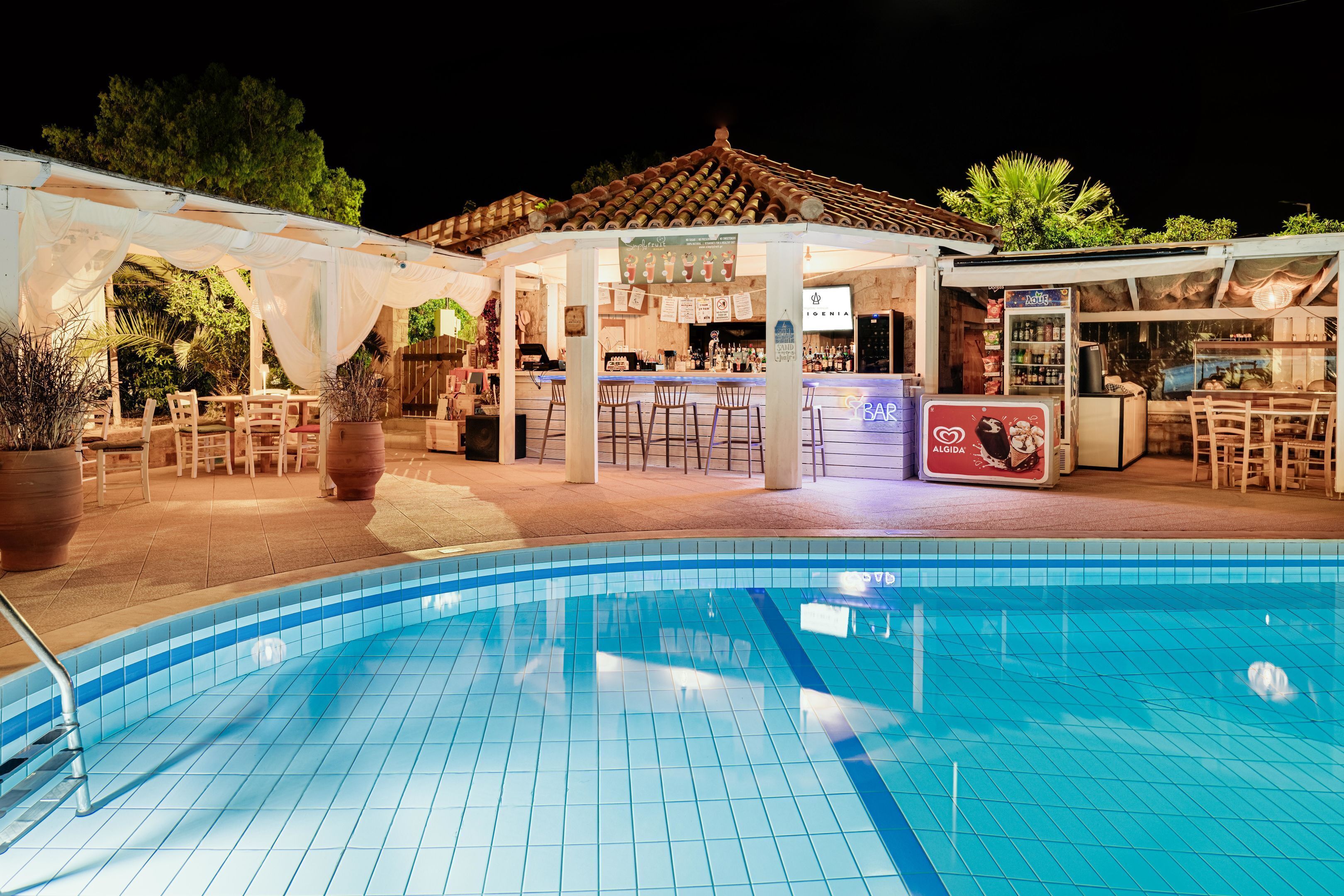Zona de bar junto a la piscina, con piscina de azulejos, mobiliario exterior y barra.
