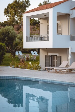 A modern two-story building with a swimming pool, outdoor seating, and a garden area. - Iphigenia Mythic Retreat (Hersonissos)