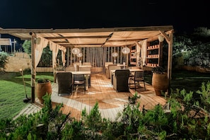 An outdoor patio with wooden flooring, wicker furniture, and hanging lights. - Iphigenia Mythic Retreat (Hersonissos)