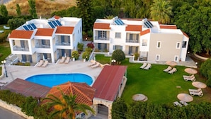 A modern multi-story building with a swimming pool, sun loungers, and solar panels. - Iphigenia Mythic Retreat (Hersonissos)