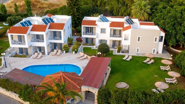 A modern multi-story building with a swimming pool, sun loungers, and solar panels. - Iphigenia Mythic Retreat (Hersonissos)