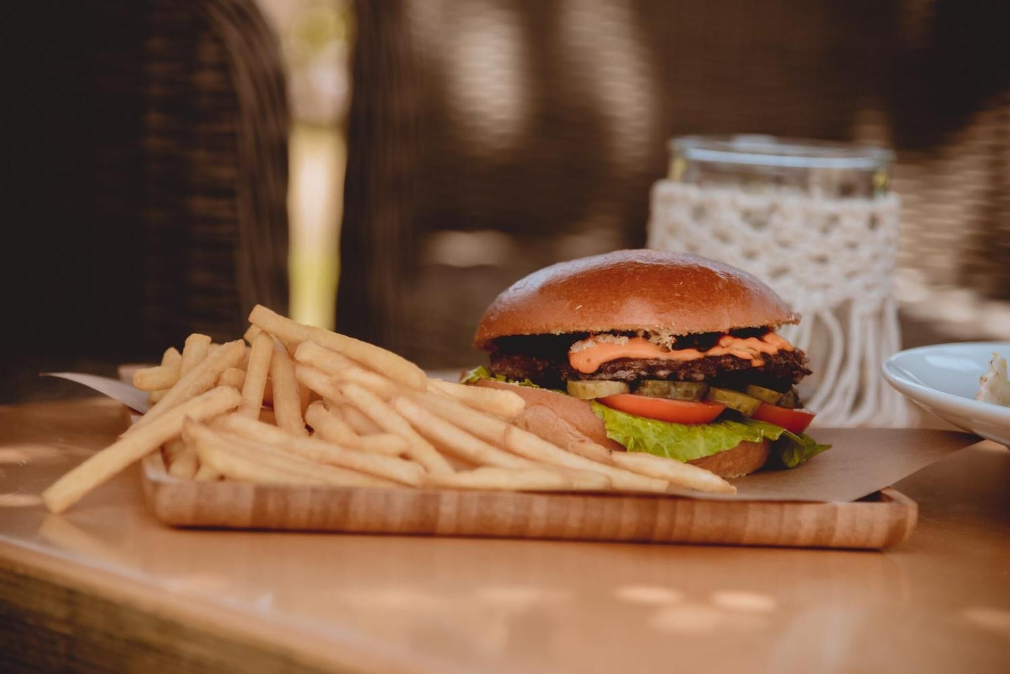 A burger with fries on a wooden board, with a glass of water in the background.