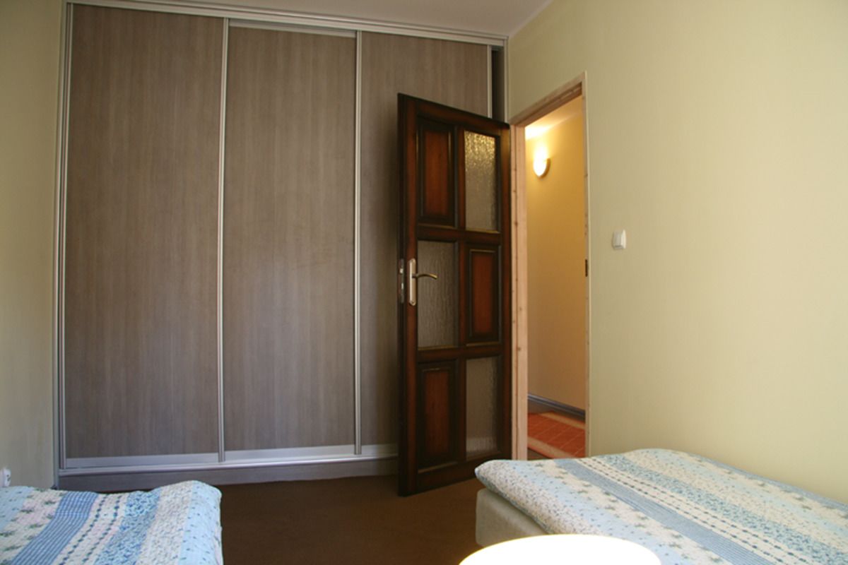 Een kamer met een schuifdeurkast, nachtkastje en een bed met een behangpatroon.