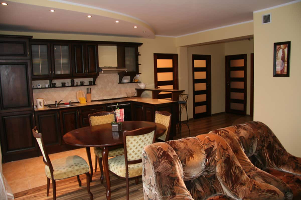 A dining area with a wooden table and chairs, a sofa, and a kitchen with dark wooden cabinets and a window.