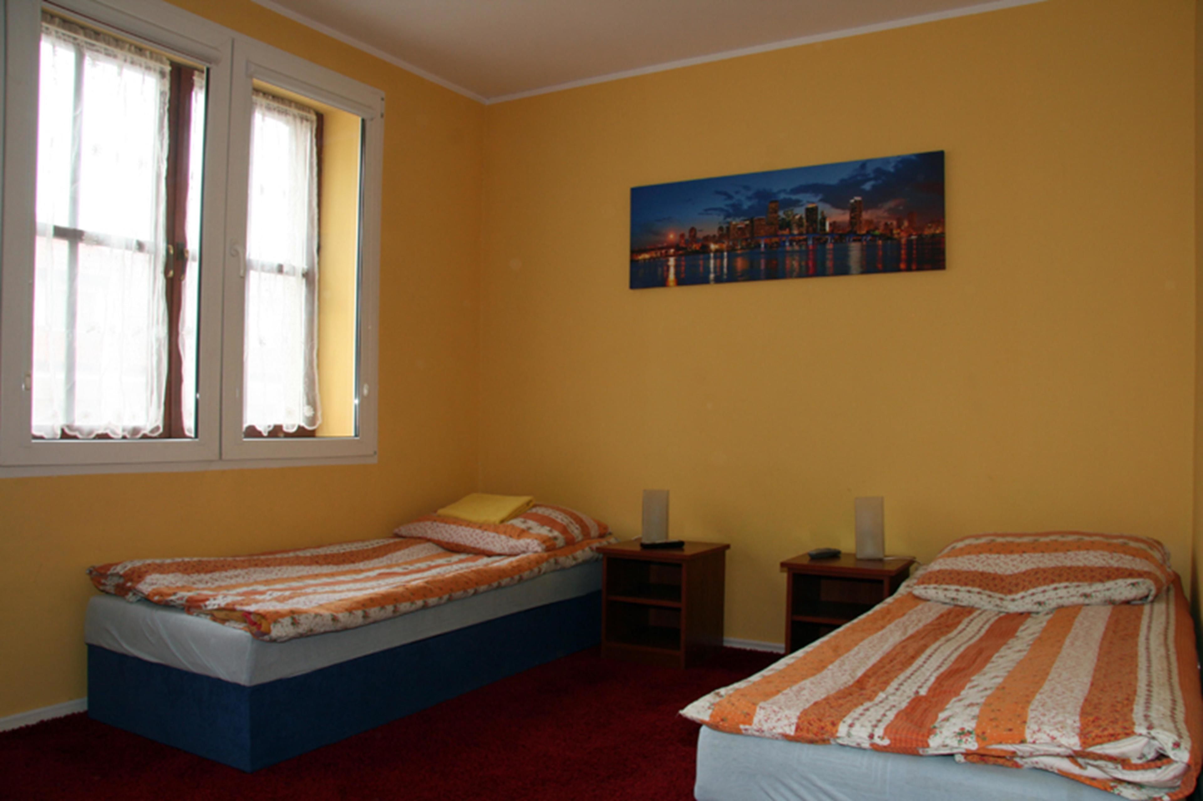 A bedroom with two beds, a cityscape painting, and a window with curtains.