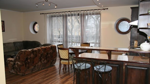 Een woonkamer met een bank, een eettafel met stoelen, en een keuken met een barstoel.