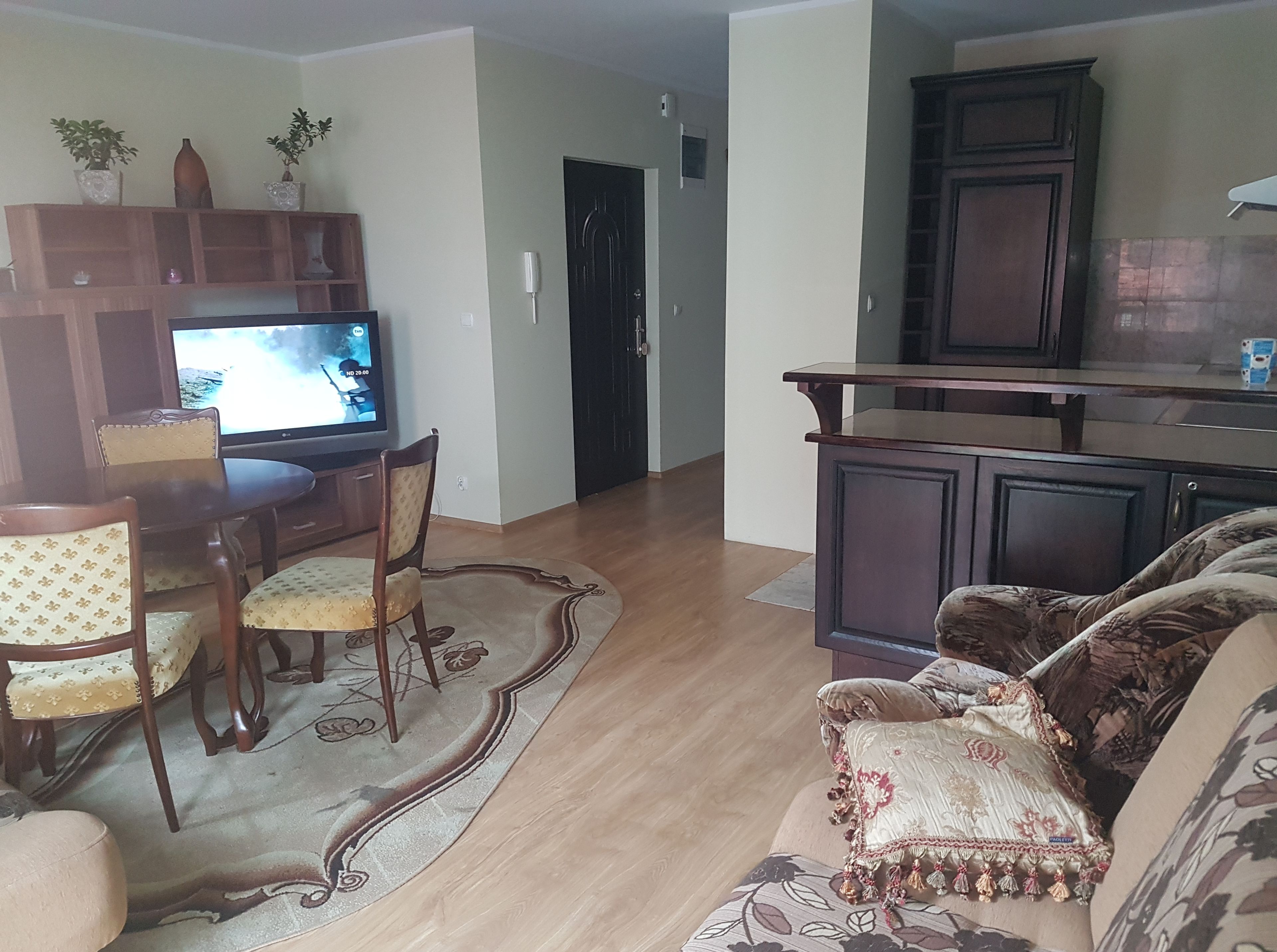 Una sala de estar con televisor, muebles de madera y una zona de cocina.