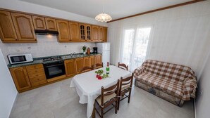 A compact kitchen with wooden cabinets, a dining table, and a checkered sofa. - Paradise Beach (Lopar)