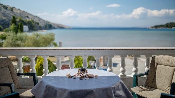 A balcony with a table set for two, overlooking a calm sea and a hilly landscape. - Paradise Beach (Lopar)
