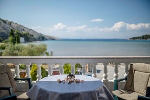 Un balcon avec une table dressée pour deux personnes, offrant une vue sur une mer calme et un paysage vallonné.