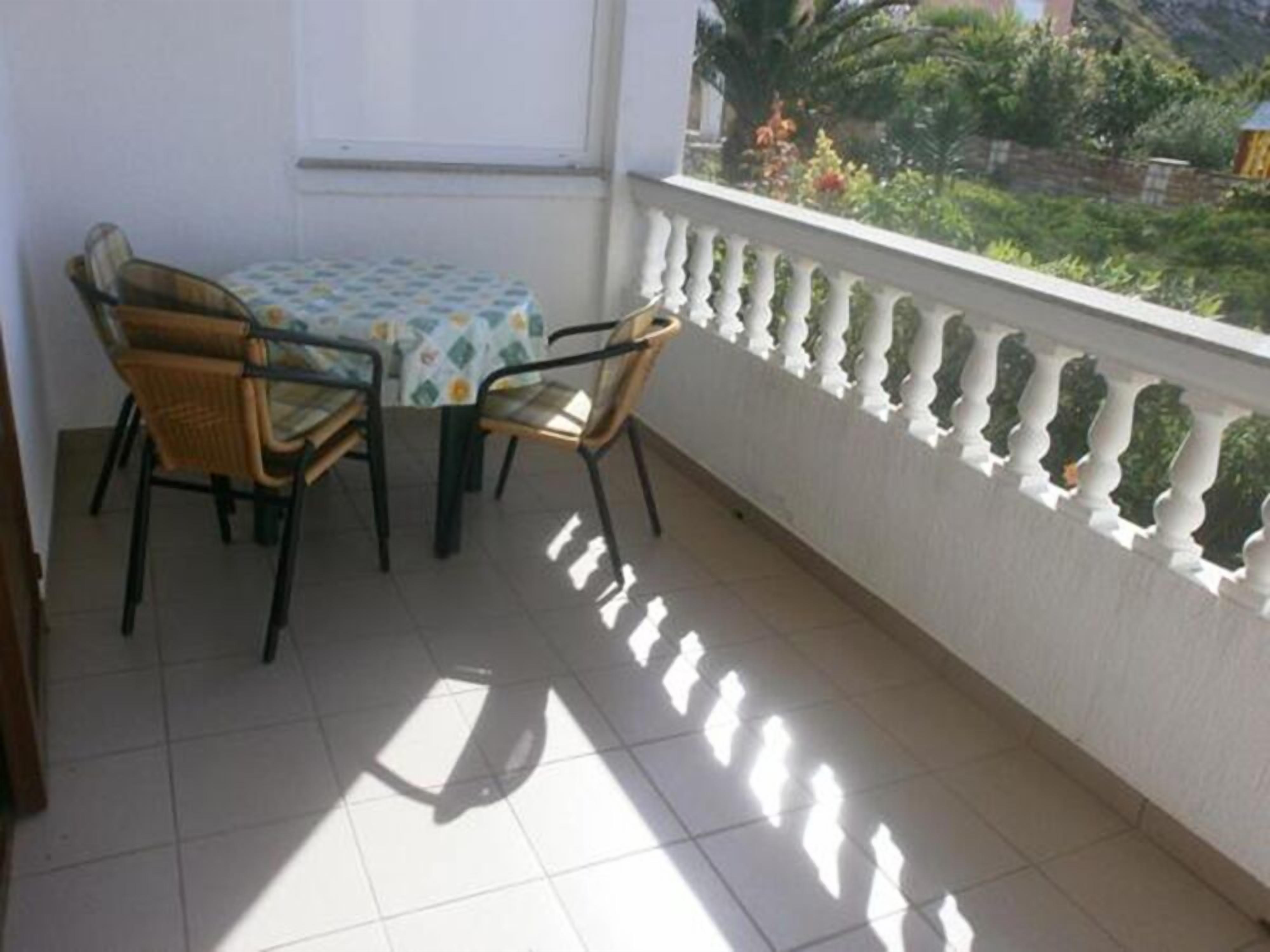 A balcony with a table and chairs, a white balustrade, and a view of greenery.