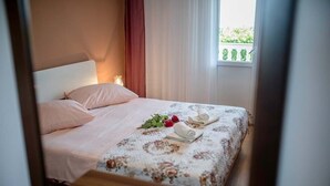 A neatly made bed with a floral bedspread, a pair of rolled towels, and a red rose on the bed. - Paradise Beach (Lopar)