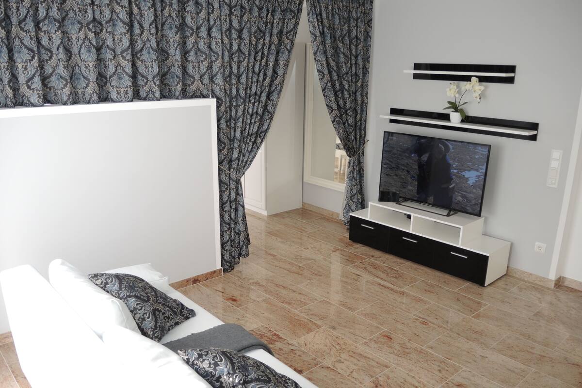 A modern living room with a white sofa, patterned cushions, a flat-screen TV, and a minimalist entertainment unit.