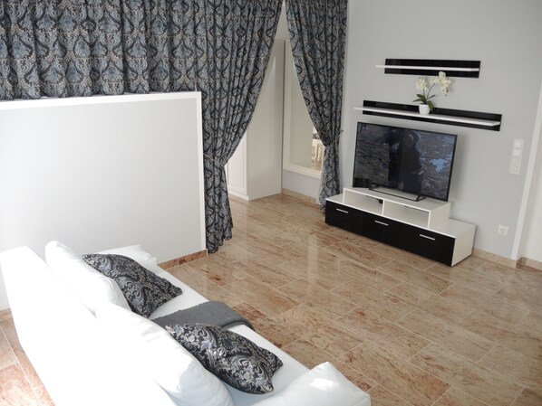 A modern living room with a white sofa, patterned cushions, a flat-screen TV, and a minimalist entertainment unit.