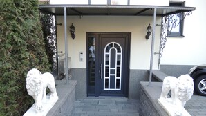 A building entrance with a black door, two stone lion statues, and a covered porch area. - Merkel Villa Apartamente (Wiesbaden)