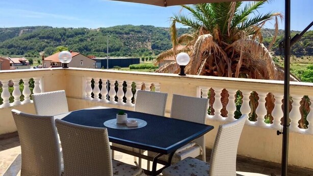 A balcony with a table and chairs, a palm tree, and a view of a hilly landscape. - Piano (Lopar)