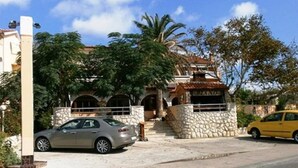 A two-story house with a stone facade, a car parked in front, and a yellow car parked on the street. - Piano (Lopar)