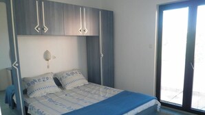 A bedroom with a bed, a wardrobe, a nightstand, and a window. - Piano (Lopar)
