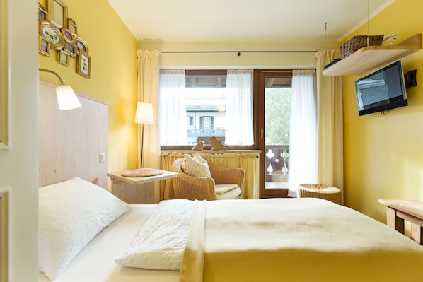 A hotel room with two beds, a television, a window with curtains, and a wicker chair. - Das Schönanger (Grainau)