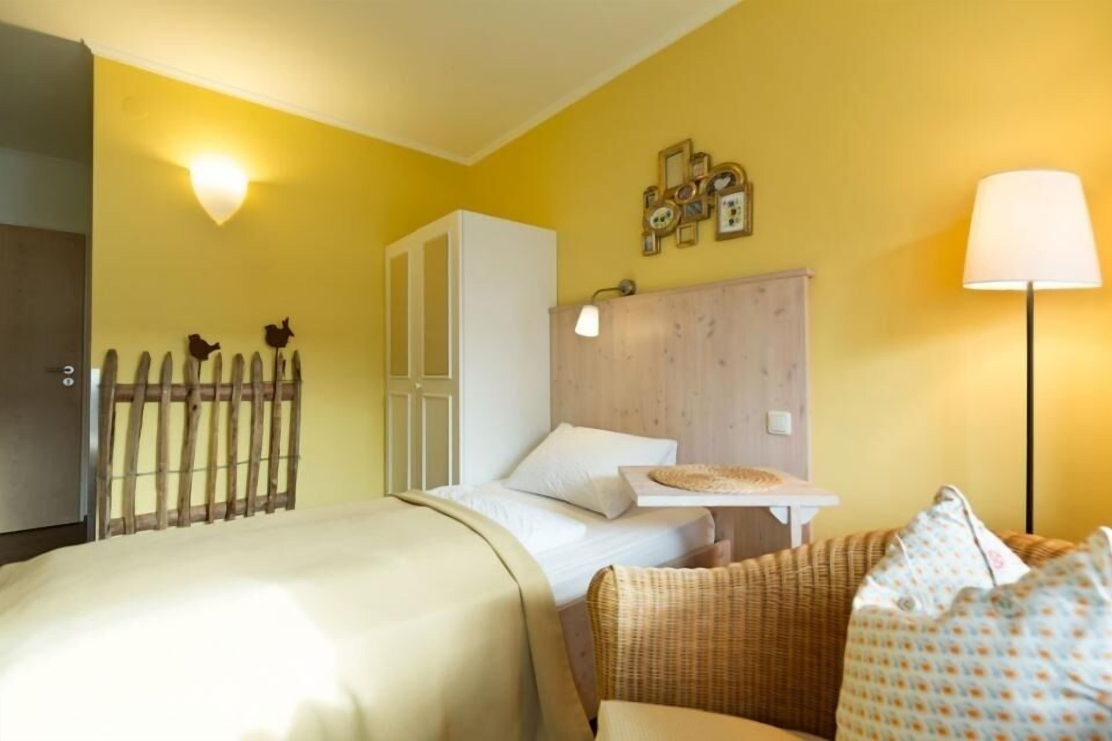 A hotel room with a bed, a wooden headboard, a nightstand, a lamp, and a wall-mounted light fixture.