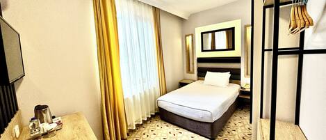 Een hotelkamer met een bed, een bureau met koffiezetapparaat, een spiegel en een kapstok.