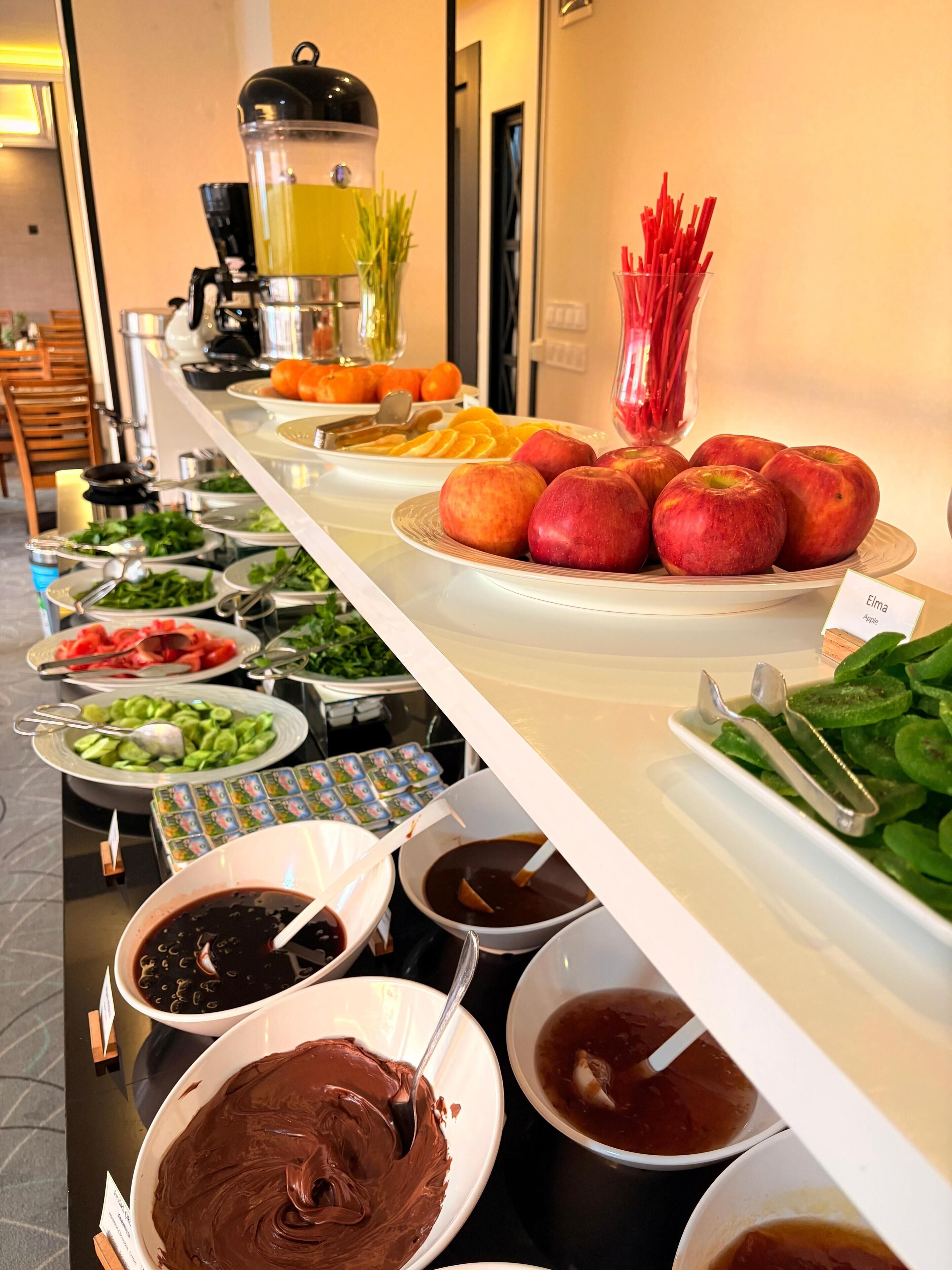 A buffet with various food items including apples, oranges, and green vegetables.