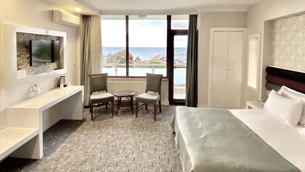Habitación de hotel con cama, escritorio, silla, televisor y vista al mar.