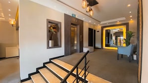 Un moderno vestíbulo de hotel con una escalera, un mostrador de recepción y un espejo que refleja el interior.