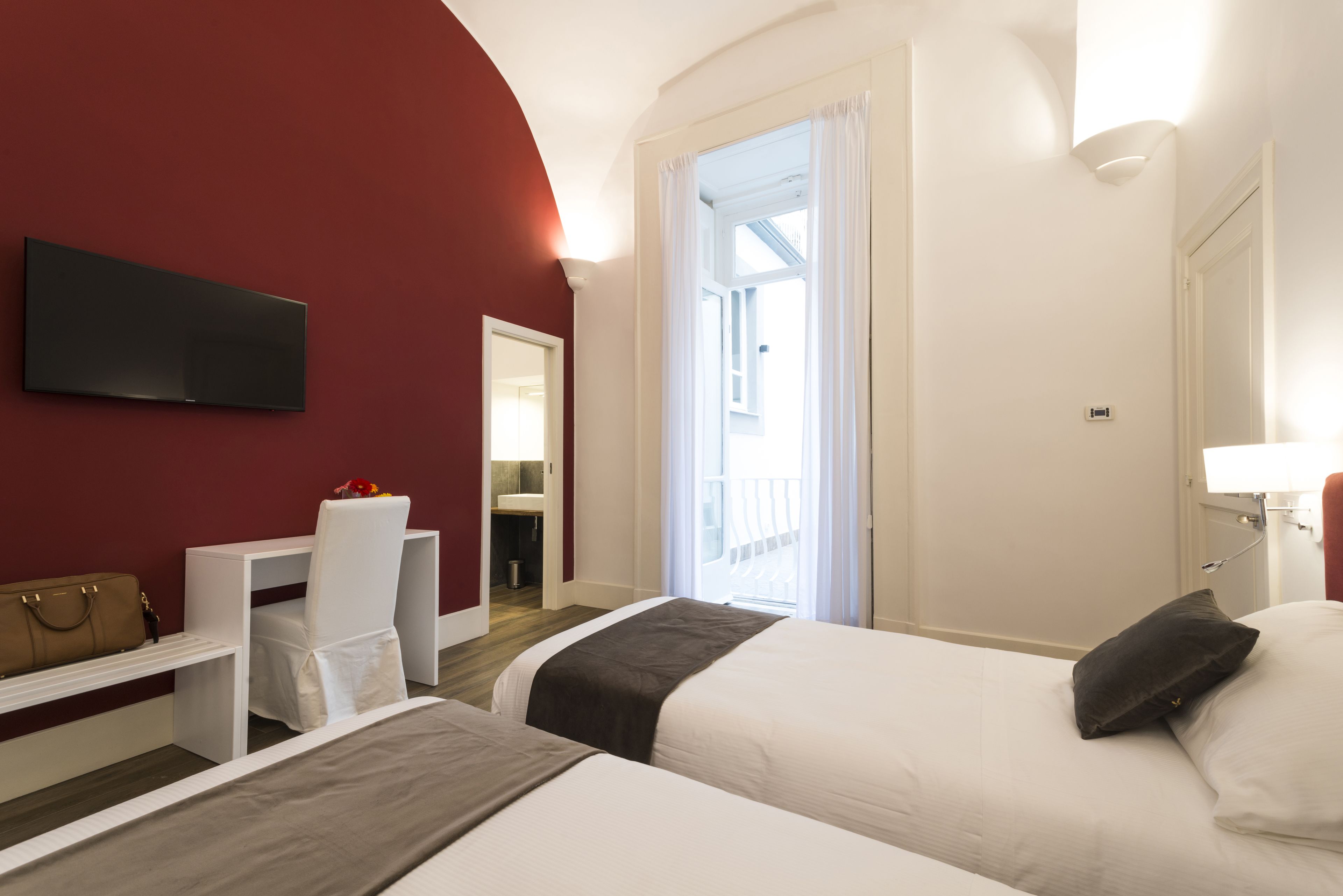 A hotel room with two beds, a desk, a chair, a TV, and a bathroom visible through an open door.