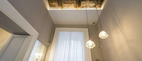 A room with a high ceiling, a large window with sheer curtains, and pendant lighting.