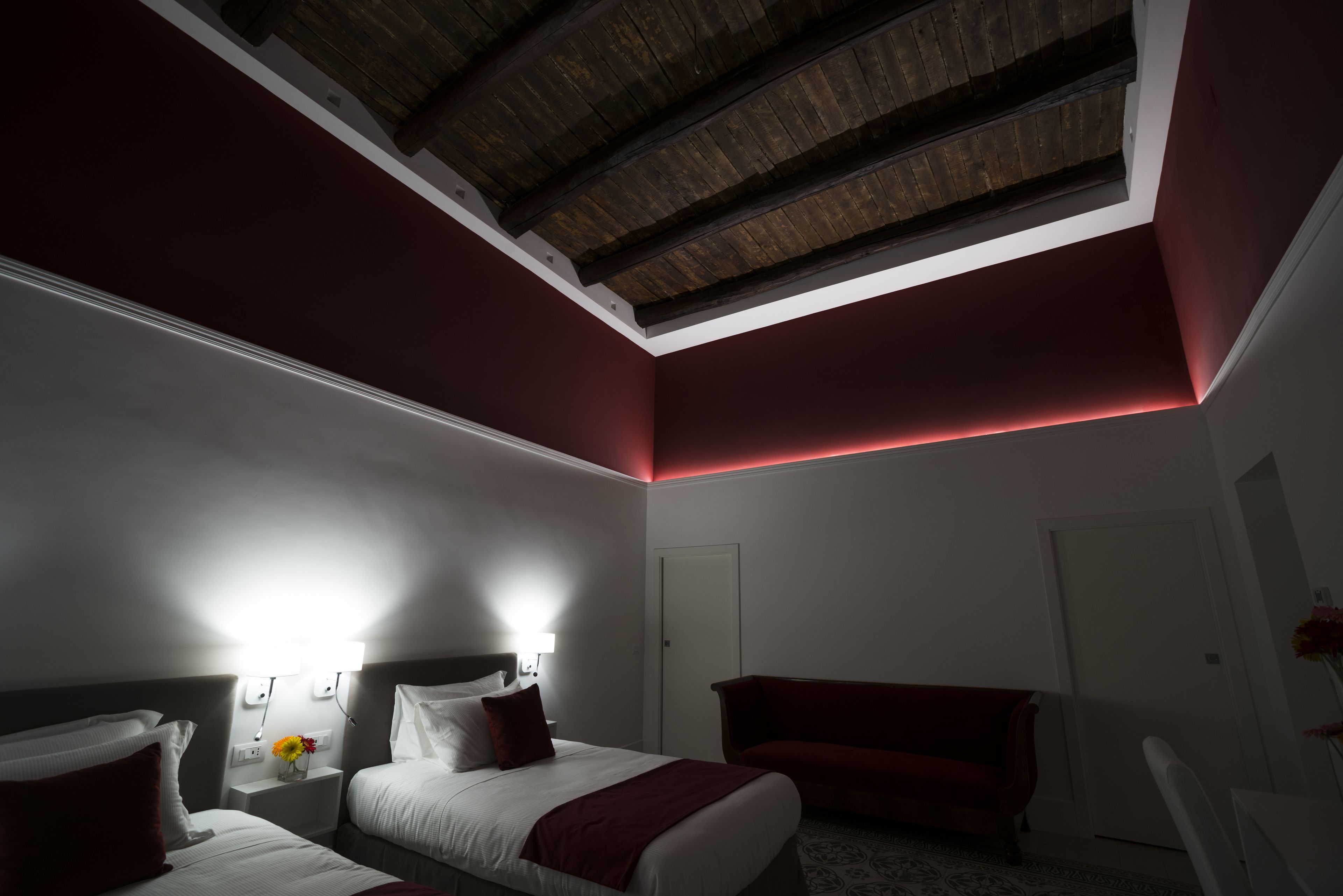 Una habitación de hotel con tragaluz, una cama, un sofá rojo y una mesita de noche con lámpara.