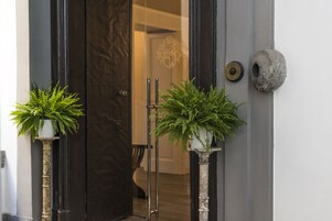 A door with a coat of arms, two potted plants, and a stone object on the wall.